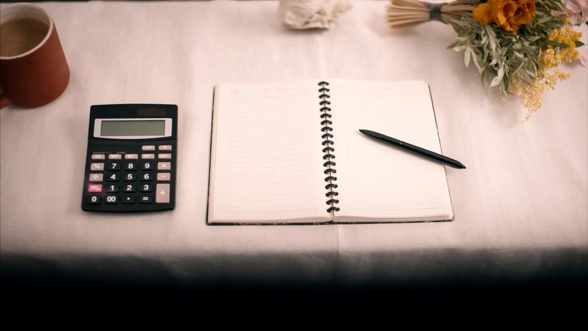 A wedding budget flat-lay with a calculator, notebook, coffee and dried flowers