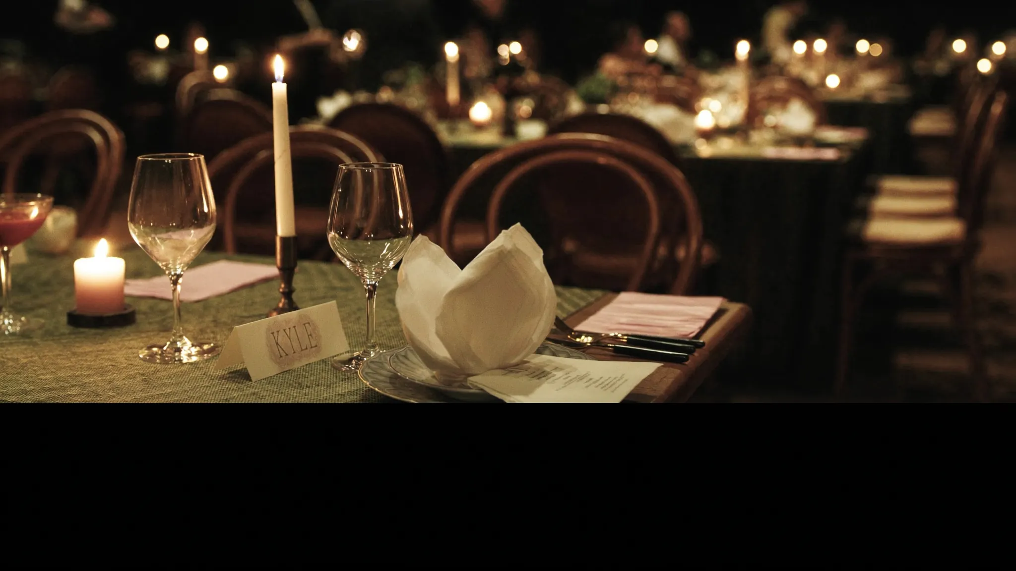 A candlelit wedding reception table set with wine glasses and a place card