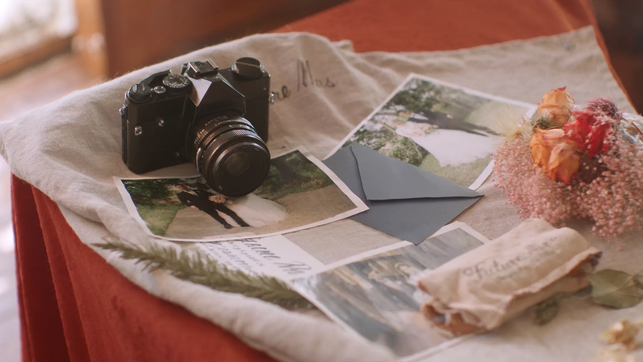 A vintage film camera resting on printed wedding photos and dried flowers