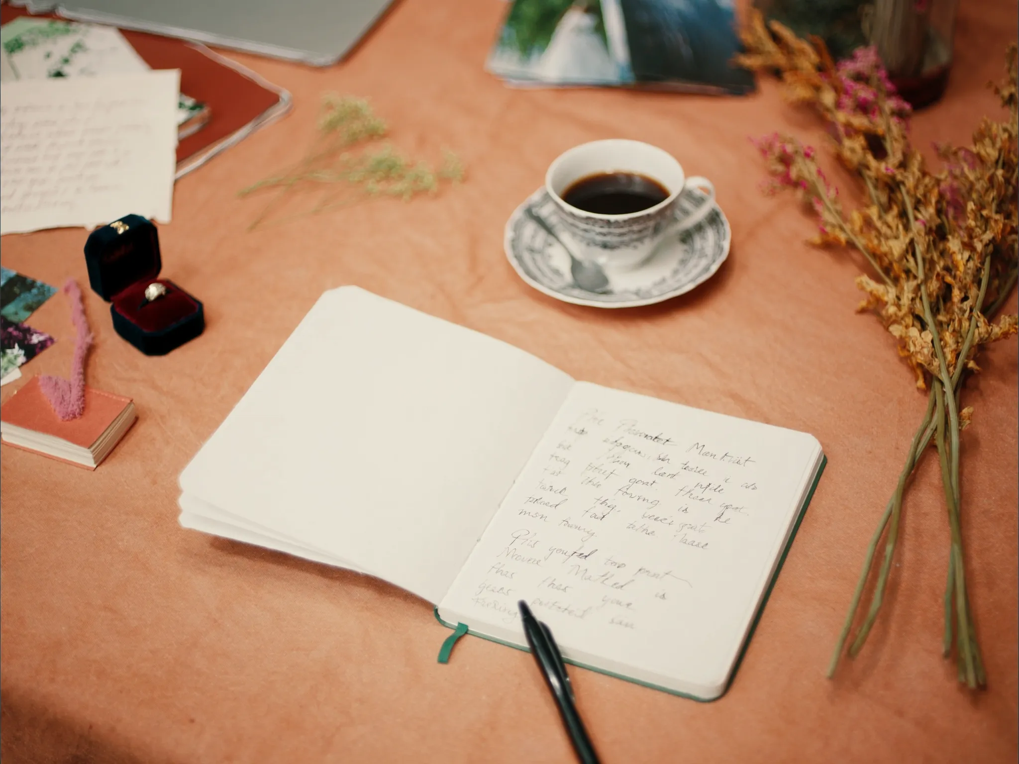 A wedding planning notebook, coffee and a ring box on a warm desk