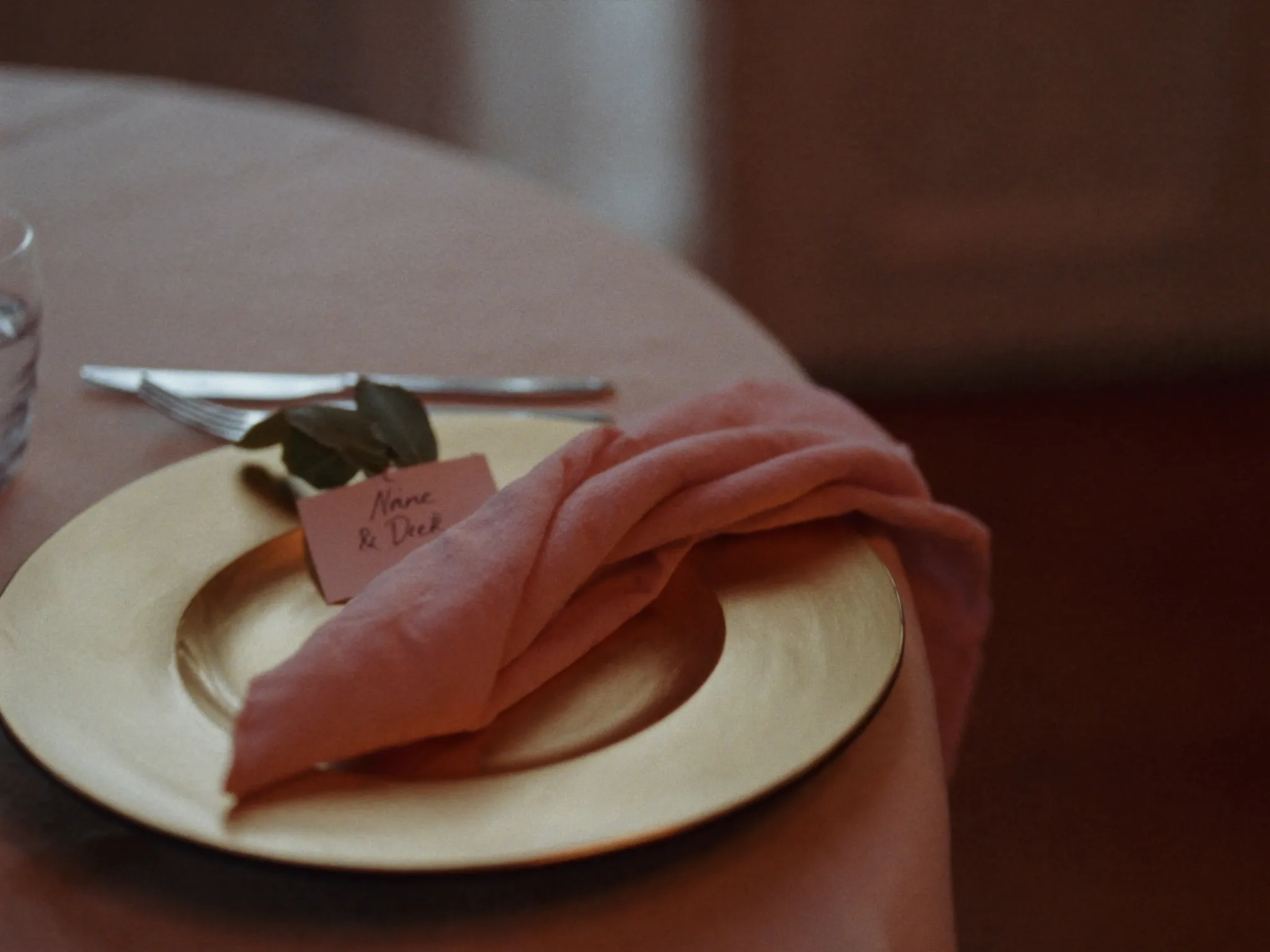 An elegant place setting with a gold charger, blush napkin and name card
