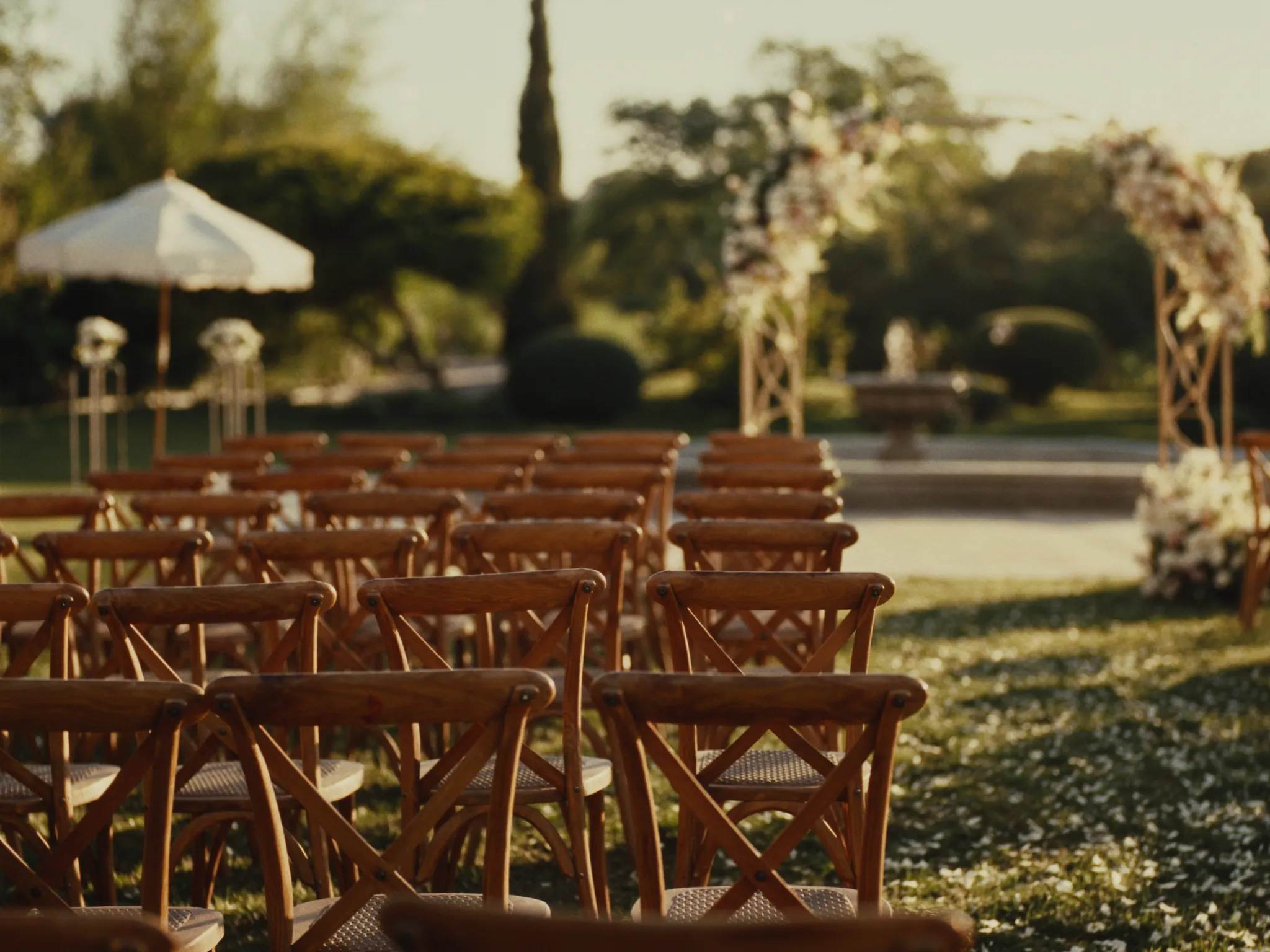 Rows of wooden ceremony chairs along a petal-strewn garden aisle at golden hour