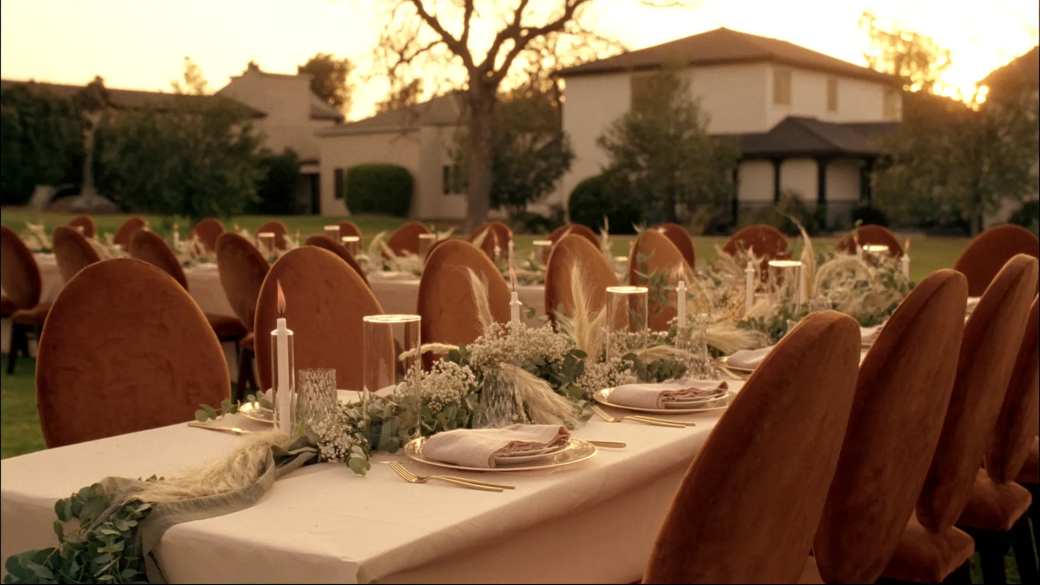 An elegant golden-hour outdoor wedding reception with terracotta velvet chairs, dried florals and candlelight